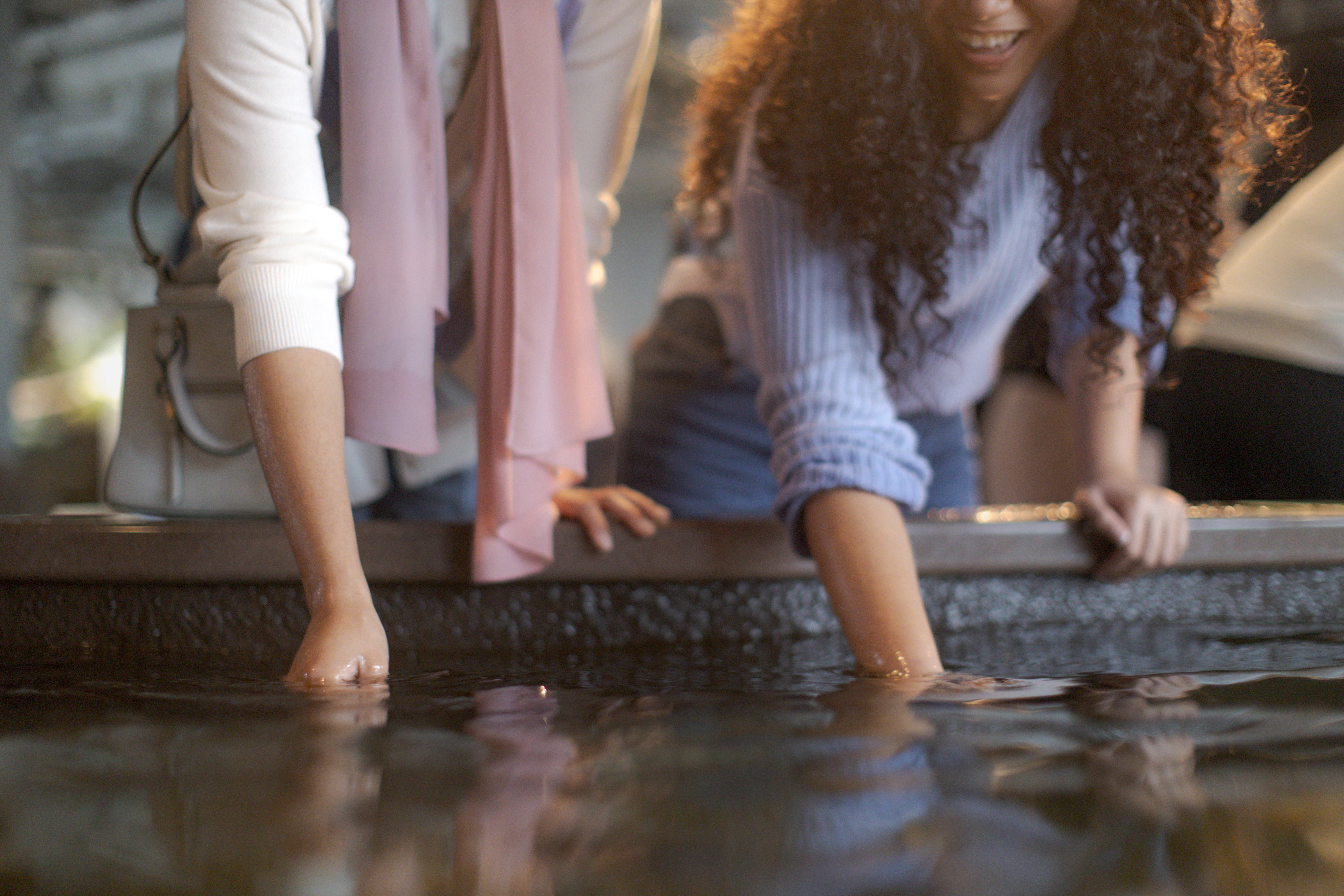 Two visitors reach into a touch pool exhibit, smiling as they interact with the water